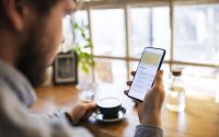 Young man tracking finance on mobile app while drinking coffee.