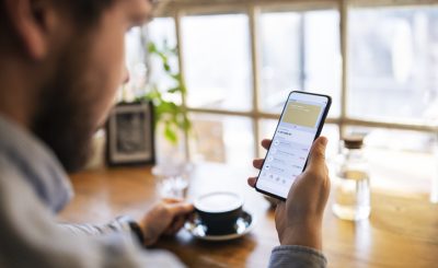 Young man tracking finance on mobile app while drinking coffee.